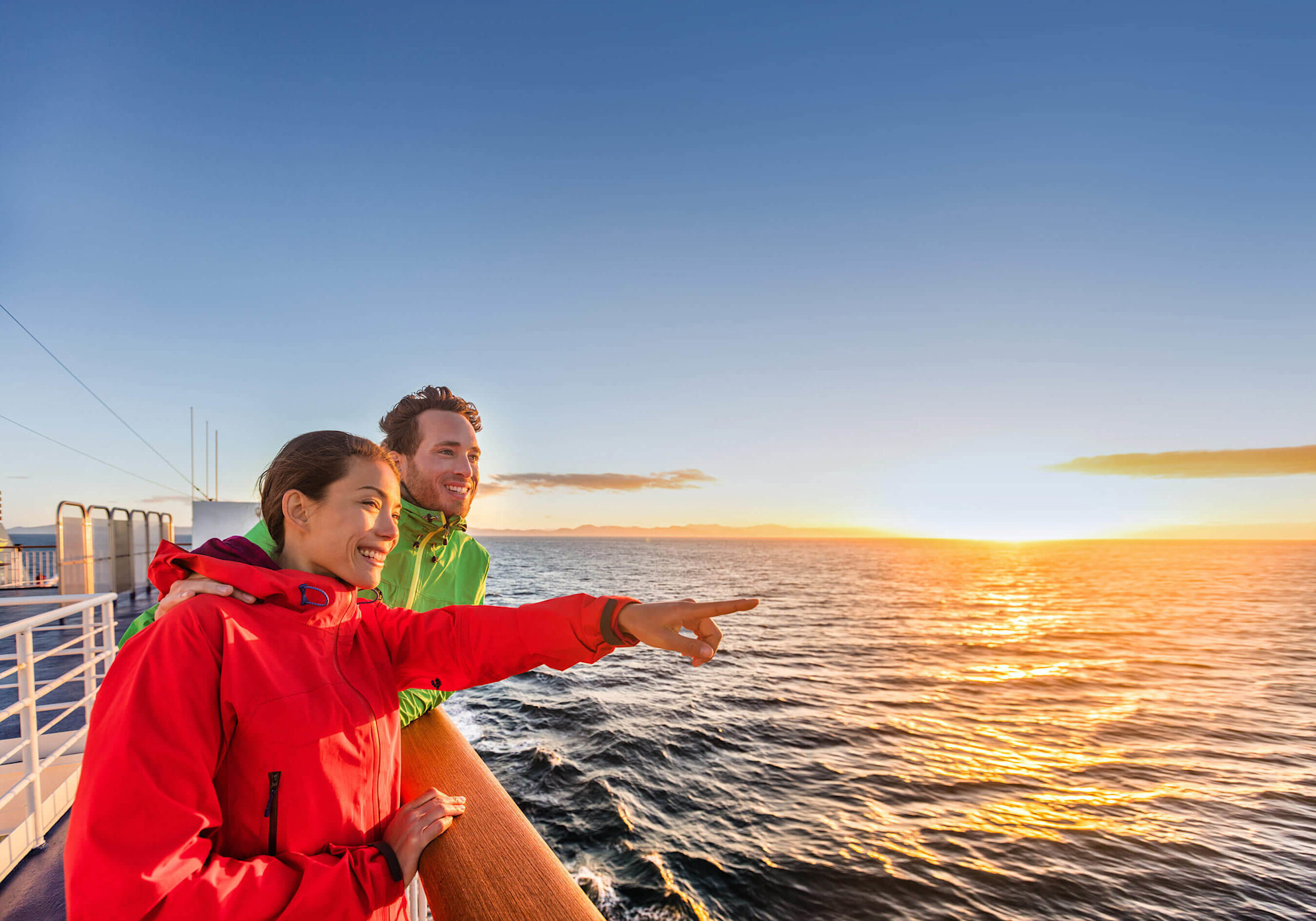 Couple on deck wearing windbreaker jackets with sunset in the background