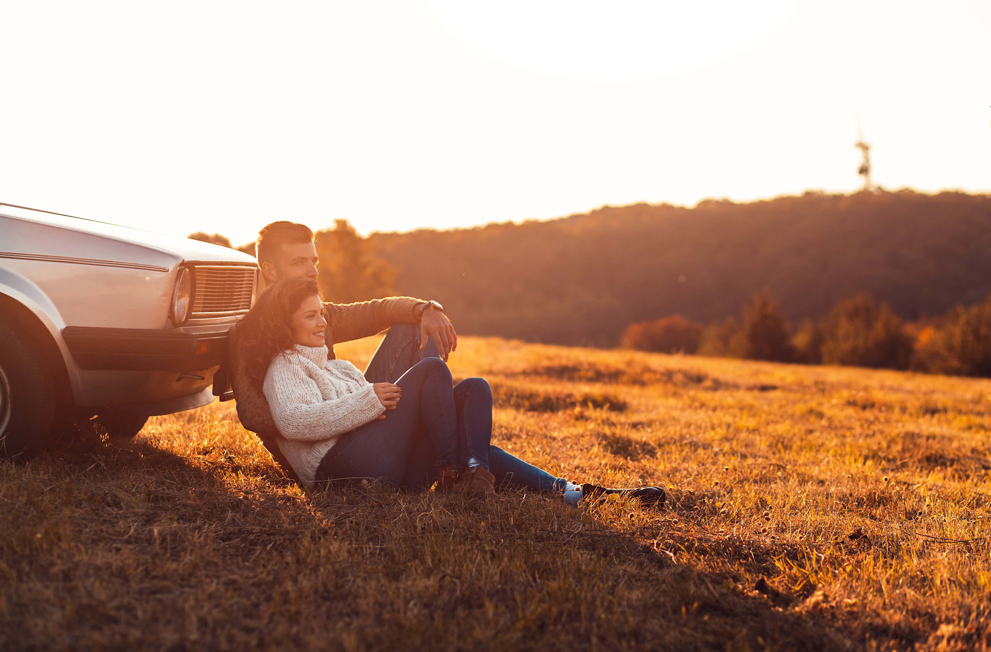 Couple sat leaning against a car in a field