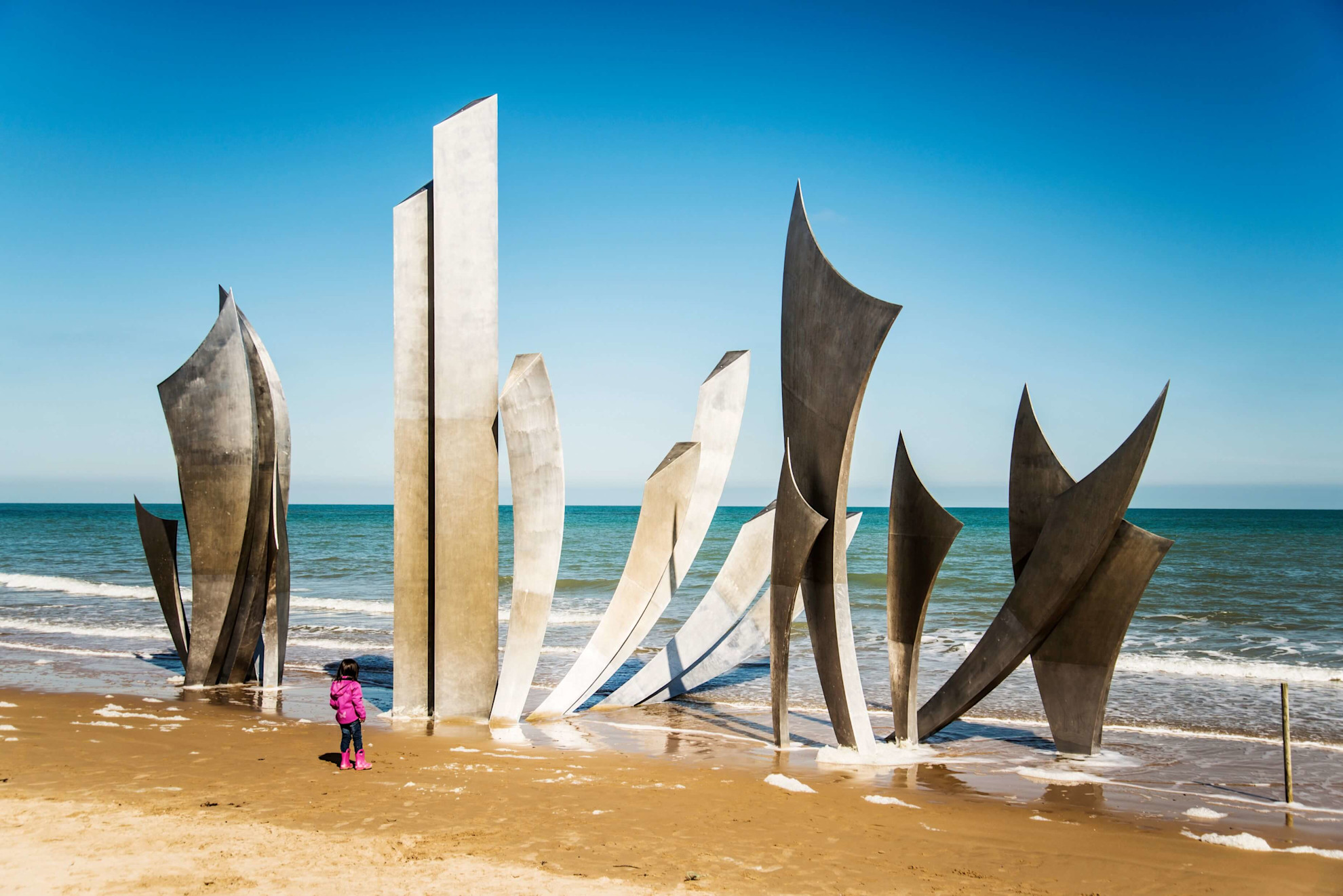 Little girl watches the waves around the Les Braves memorial at Omaha Beach