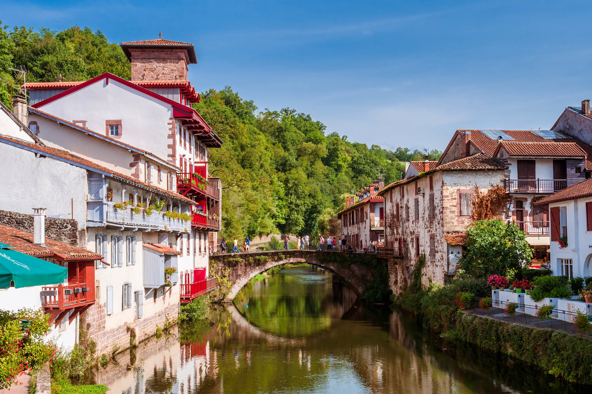 Saint-Jean-Pied-de-Port: A picturesque white town with red balconies, flowers, and a serene river.