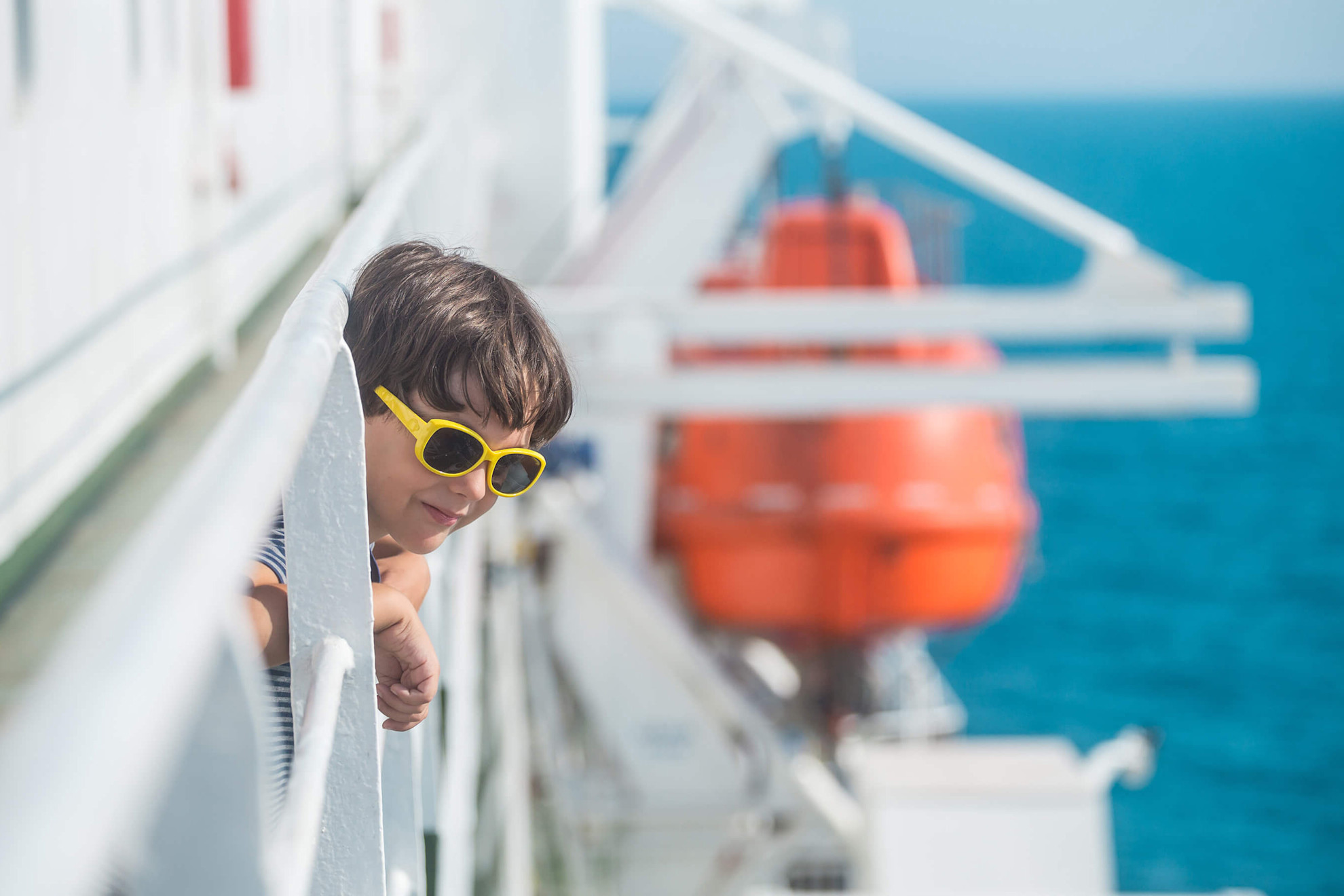 A boy wearing sunglasses on deck looking out to sea
