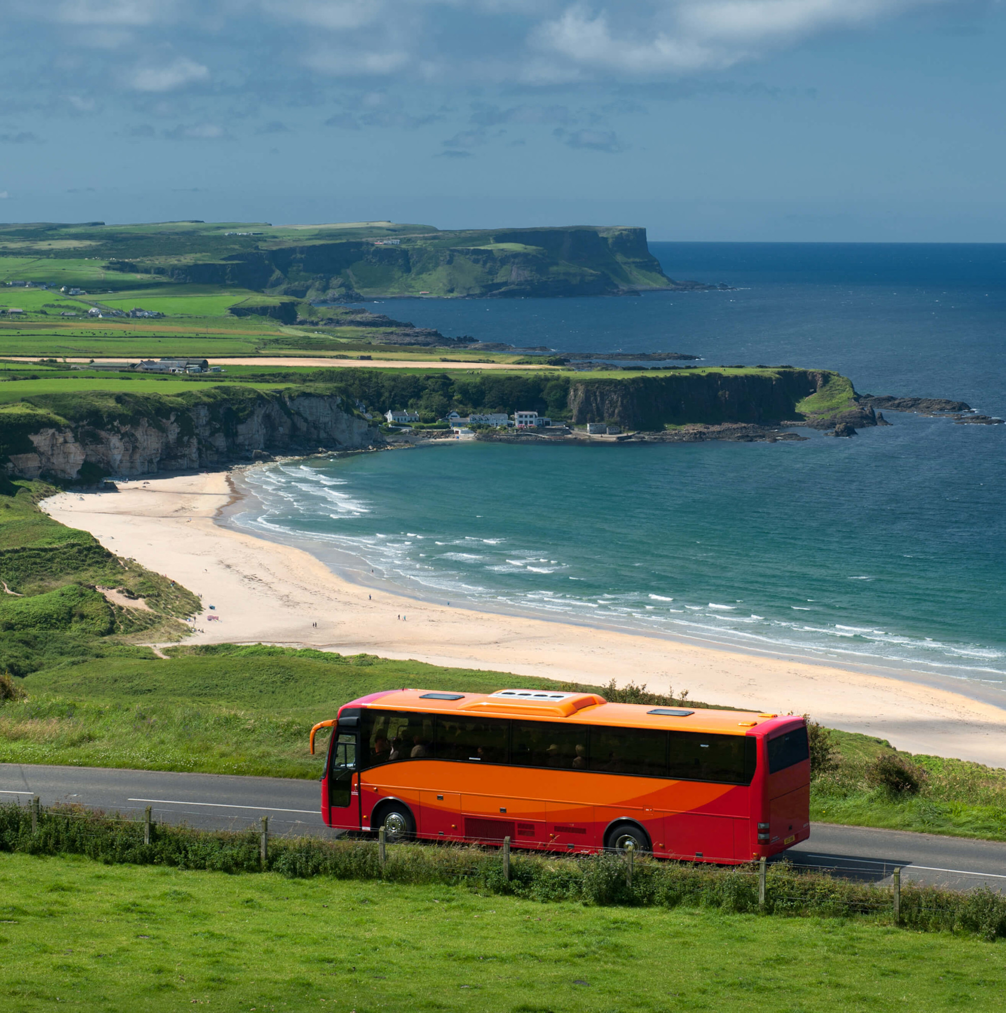 A coach on a coastal road with a beautiful beach in the background