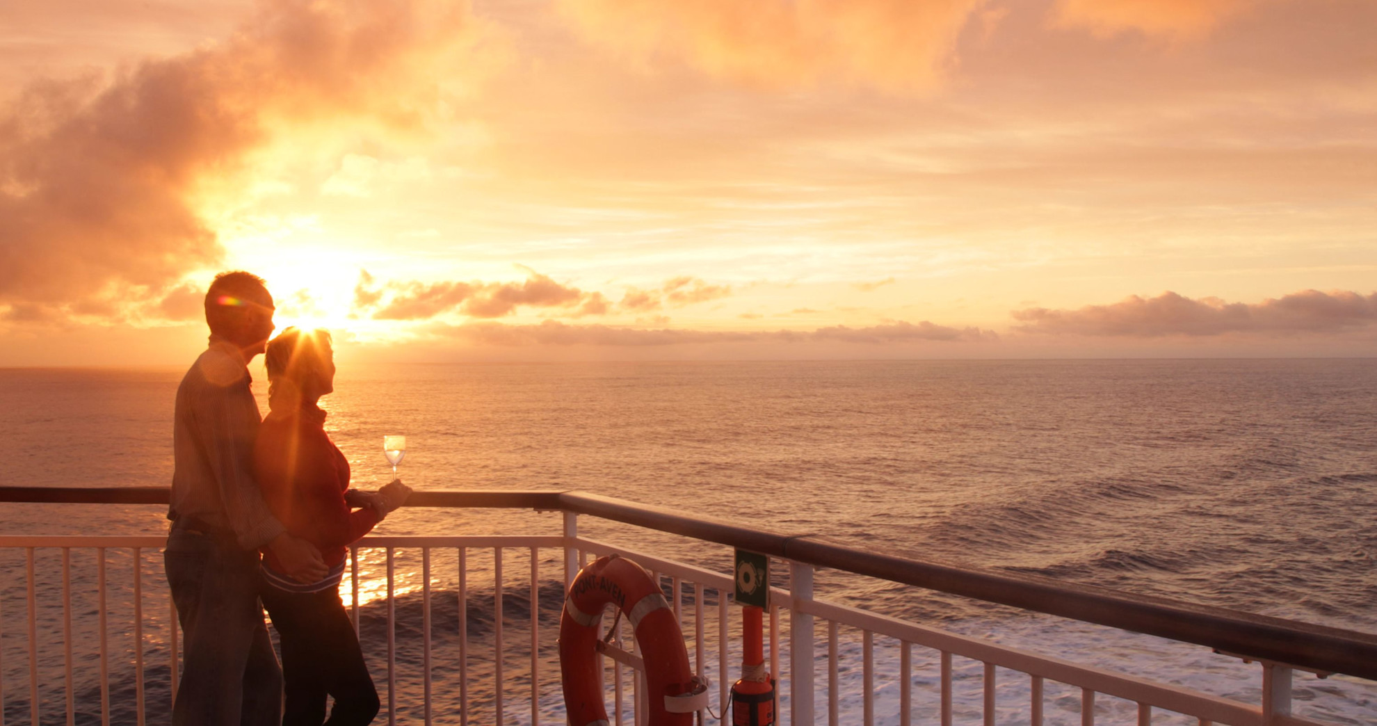 Couple on deck at sunset with glasses of wine