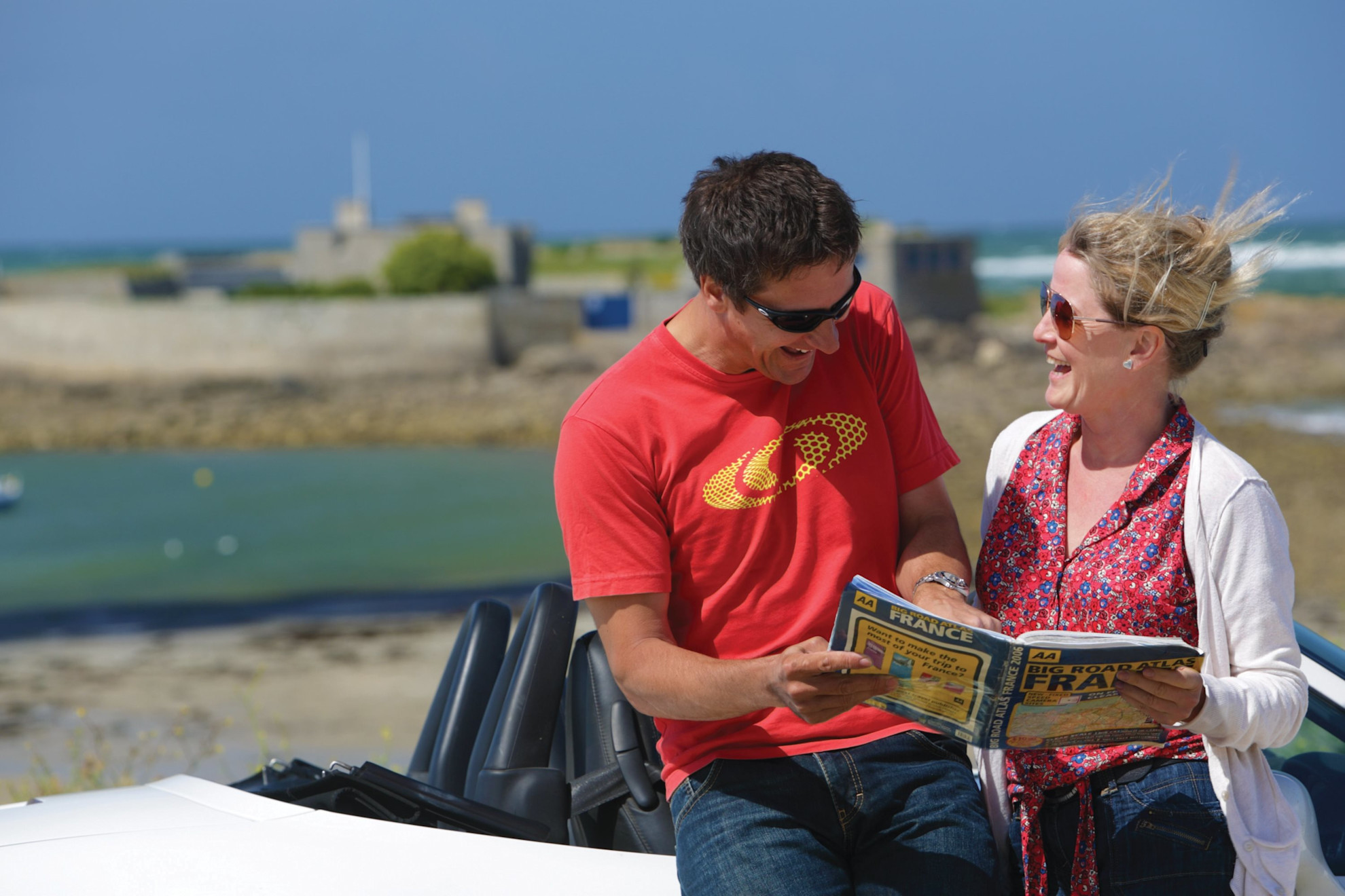 A man and a woman reading by their car